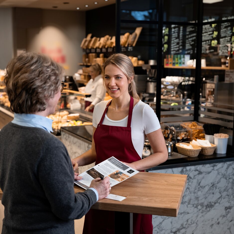 Přátelská interakce mezi zákazníkem a personálem kavárny, zdůraznění možností nabídky a pozorná obsluha.