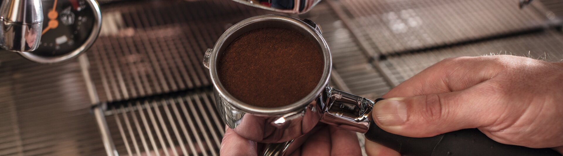 Barista préparant le marc de café dans un portafiltre pour une machine à expresso sur un comptoir en acier inoxydable.
