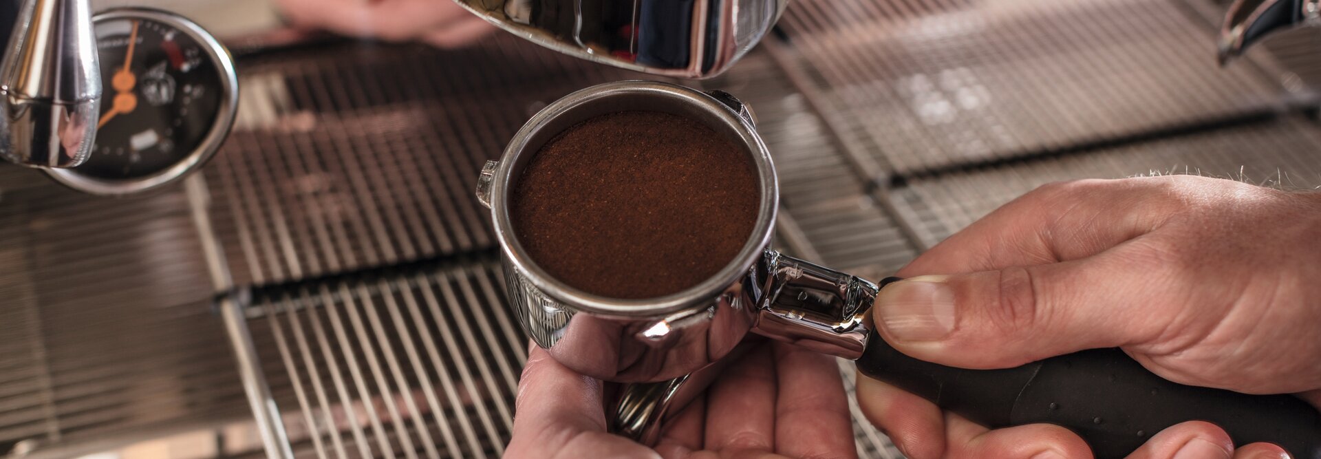 Barista préparant le marc de café dans un portafiltre pour une machine à expresso sur un comptoir en acier inoxydable.
