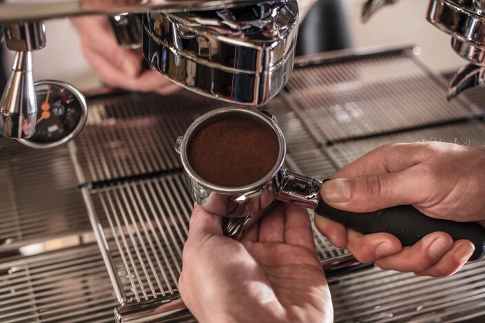Barista bereitet Kaffeesatz in einem Siebträger für eine Espressomaschine auf einer Arbeitsplatte aus Edelstahl zu.