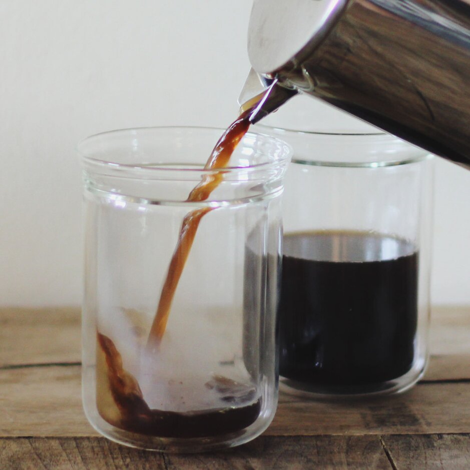 Café filtre fraîchement infusé versé dans un verre, mettant en valeur la richesse des couleurs et de la texture sur une surface en bois.
