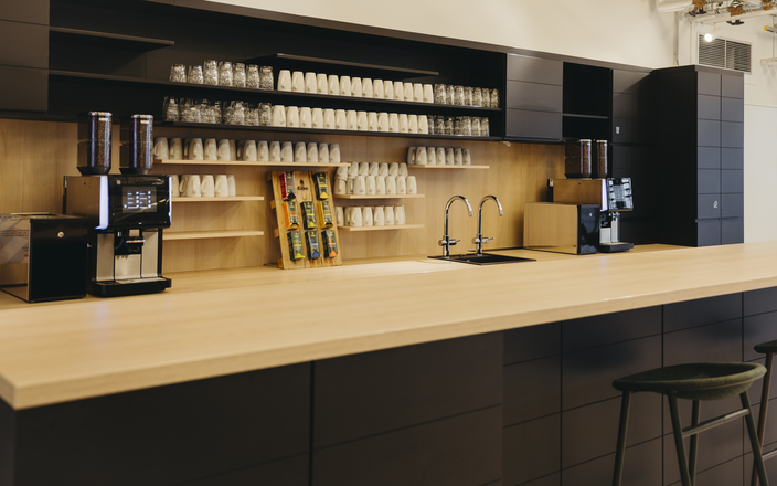 Stylish coffee station featuring sleek countertops, glassware, and coffee machines in a modern workspace setting.