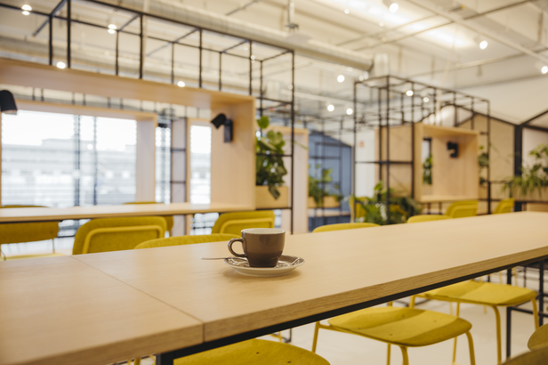 Stilvolles Café-Interieur mit einem gelben Stuhl und einer Tasse Kaffee auf einem Holztisch, mit modernem Dekor und Grünpflanzen.