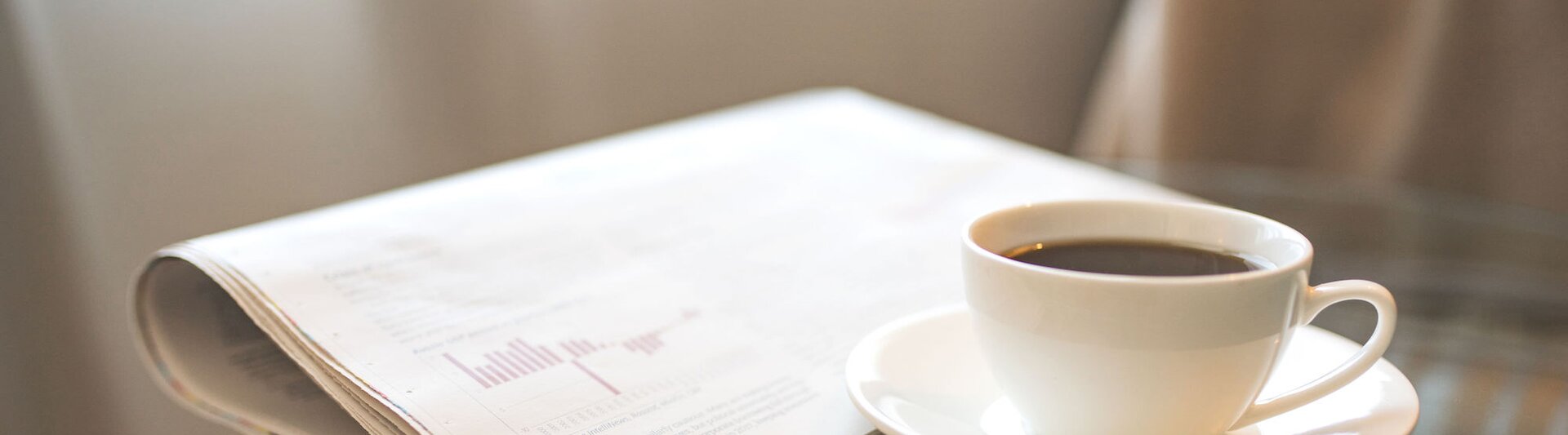 Freshly brewed coffee beside a newspaper, perfect for a morning of reading and updates on professional news.