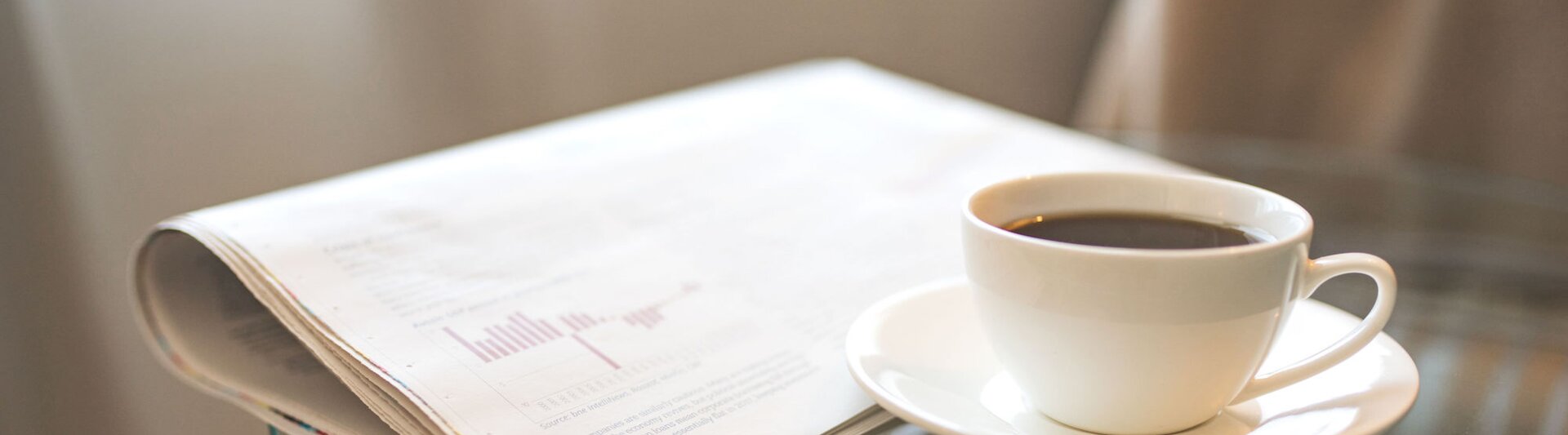 Un café fraîchement préparé à côté d'un journal, idéal pour une matinée de lecture et de mise à jour sur l'actualité professionnelle.