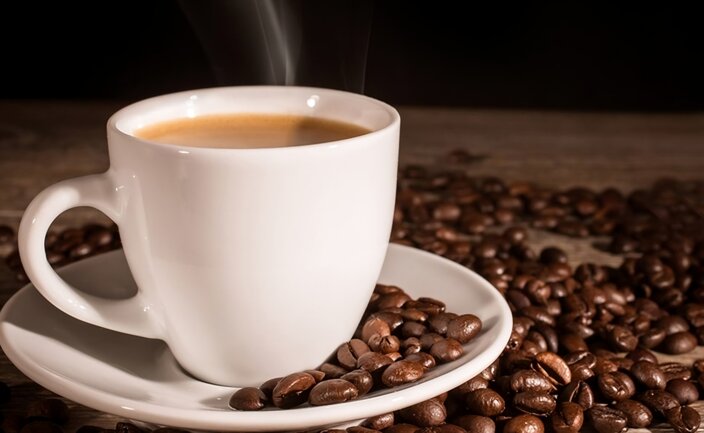 Freshly brewed coffee in a white cup, surrounded by roasted coffee beans on a rustic wooden surface.