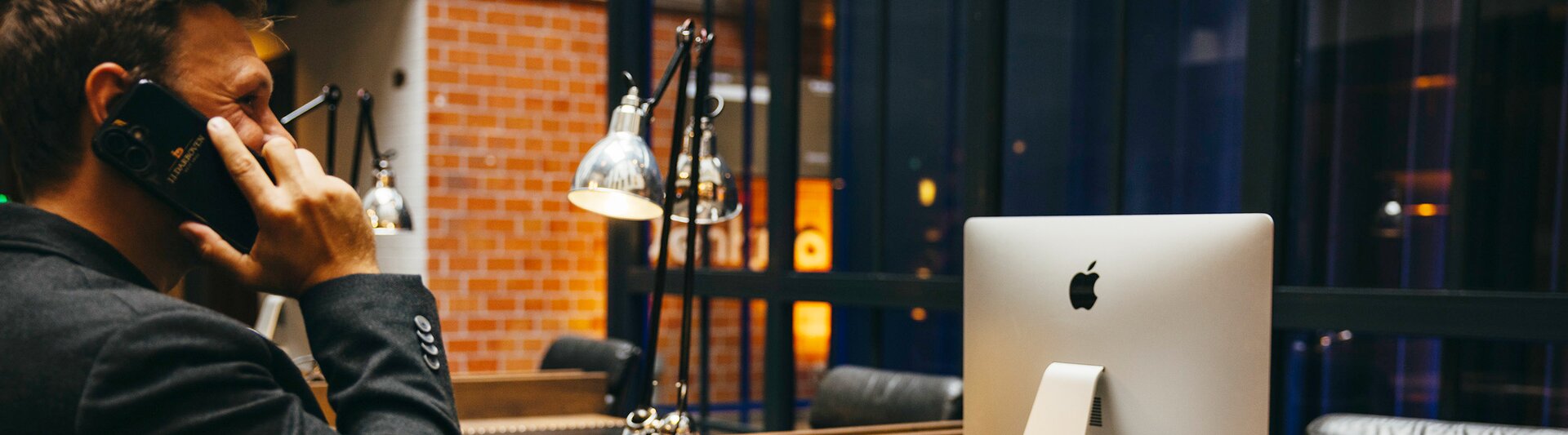 A professional man on the phone at a sleek desk, featuring an Apple computer and a coffee cup in a modern workspace.
