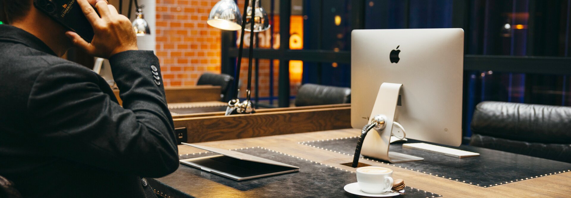 Ein professioneller Mann am Telefon an einem eleganten Schreibtisch mit einem Apple-Computer und einer Kaffeetasse in einem modernen Arbeitsbereich.