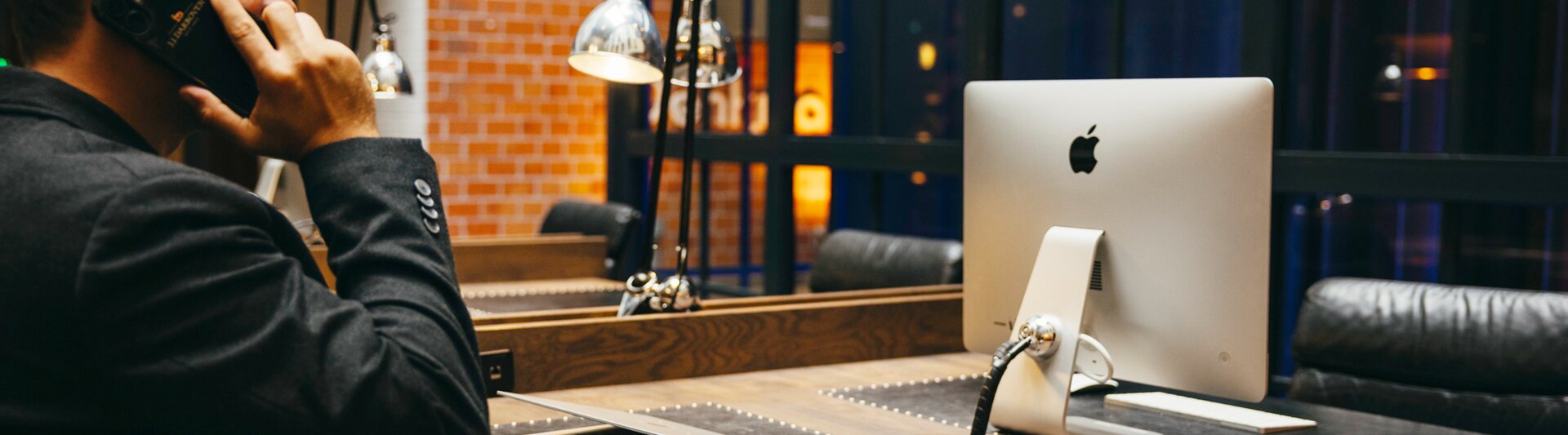 Ein professioneller Mann am Telefon an einem eleganten Schreibtisch mit einem Apple-Computer und einer Kaffeetasse in einem modernen Arbeitsbereich.