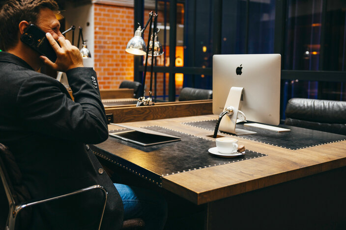 A professional man on the phone at a sleek desk, featuring an Apple computer and a coffee cup in a modern workspace.