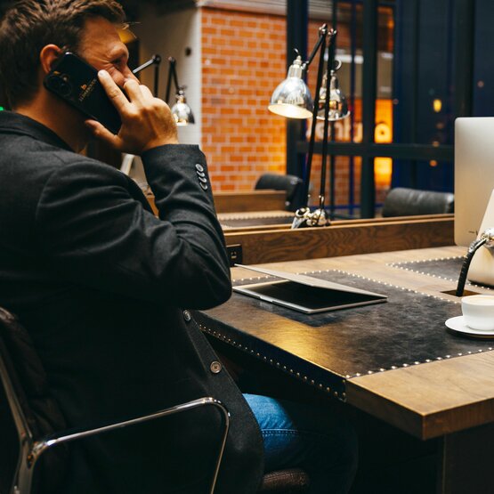 A professional man on the phone at a sleek desk, featuring an Apple computer and a coffee cup in a modern workspace.