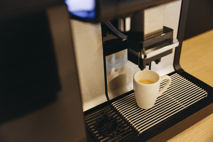 Espresso machine brewing a cup of coffee in a modern kitchen setting. Stainless steel design complements a wooden surface.