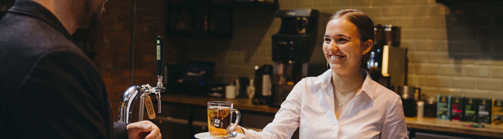 Barista serveert een kopje thee aan een klant in een stijlvol café met een gezellige sfeer.