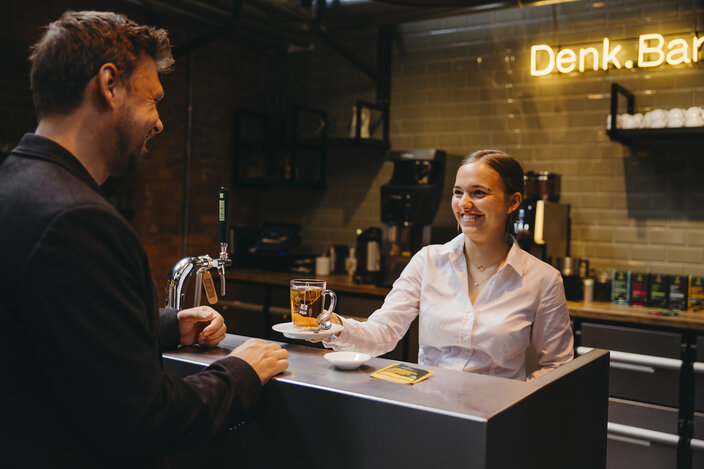 Barista serving a cup of tea to a customer at a stylish café with a welcoming atmosphere.