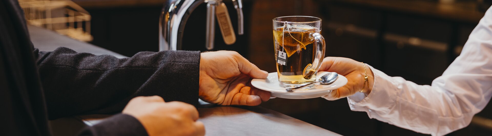 A barista serves a steaming cup of tea to a customer at a modern café, highlighting a warm beverage experience.