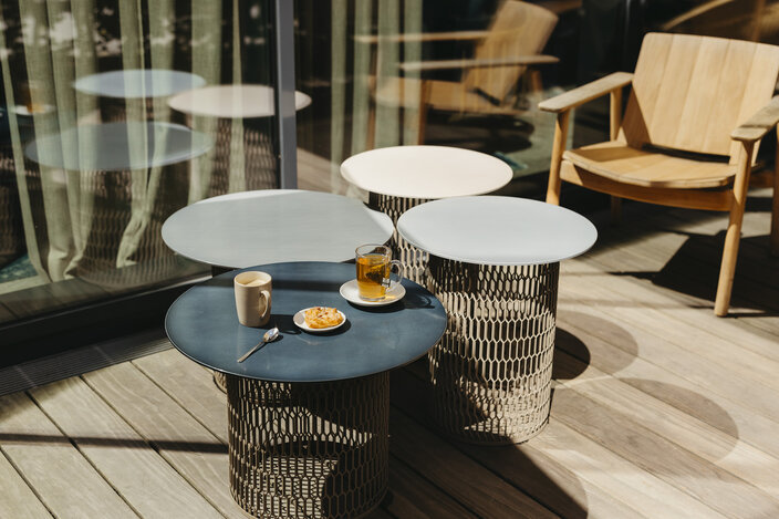 Stylish outdoor seating area with coffee, tea, and pastries on modern tables, perfect for relaxation in the sun.