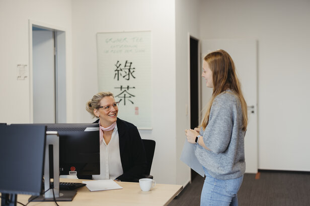 Une femme professionnelle sourit à un collègue dans un bureau, promouvant ainsi une atmosphère de travail collaboratif.