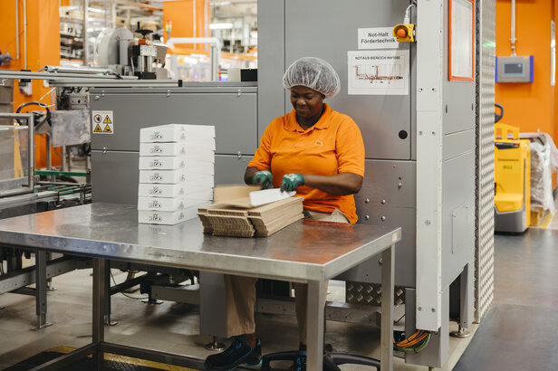 Pracownik montujący pudełka do pakowania w tętniącym życiem magazynie, pokazujący wydajne operacje przemysłowe.