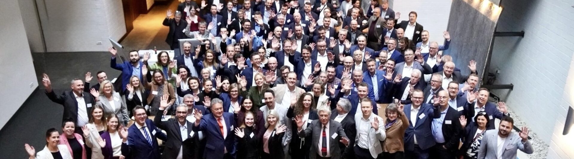 Netwerkevenement met verschillende professionals, zwaaiend en lachend, in een moderne locatie met een ontspannen sfeer.