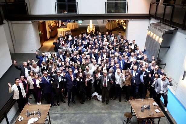 Networking event with diverse professionals, waving and smiling, in a modern venue with a relaxed atmosphere.