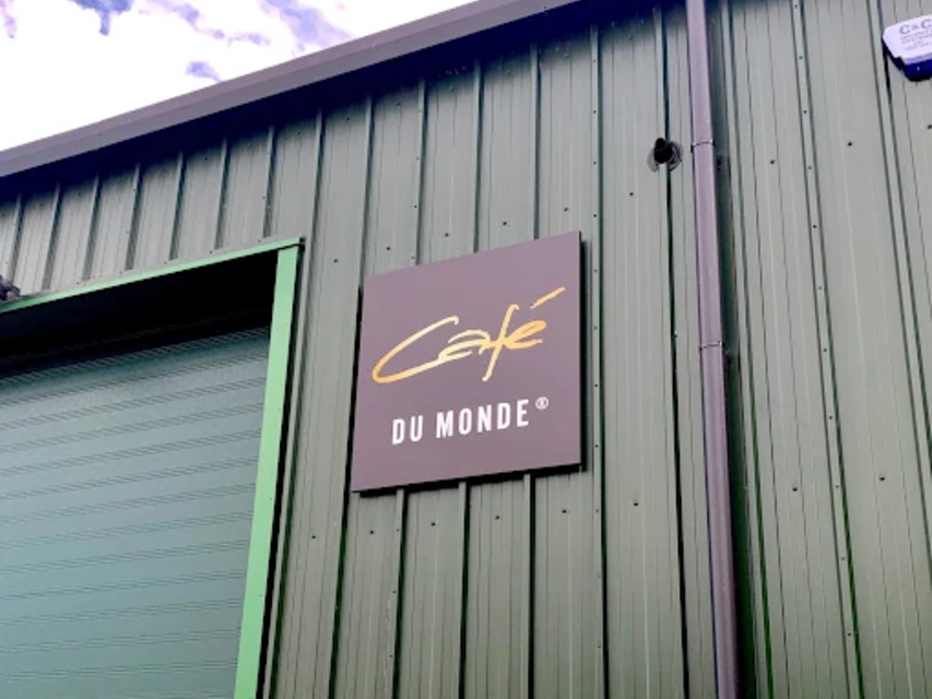 Café du Monde sign on a green building with a blue sky backdrop, iconic for its coffee and beignets in New Orleans.