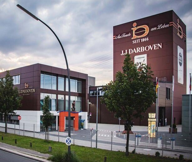 Le siège de J.J. Darboven présente une architecture moderne au milieu des arbres et des lampadaires, mettant en valeur l'histoire de la marque depuis 1866.