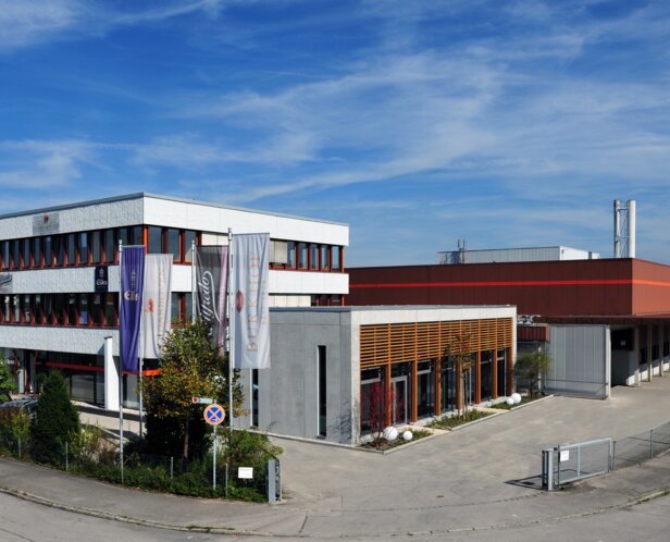 Bâtiment industriel moderne à Sauerlach, comprenant des bureaux et une usine, sous un ciel bleu clair.