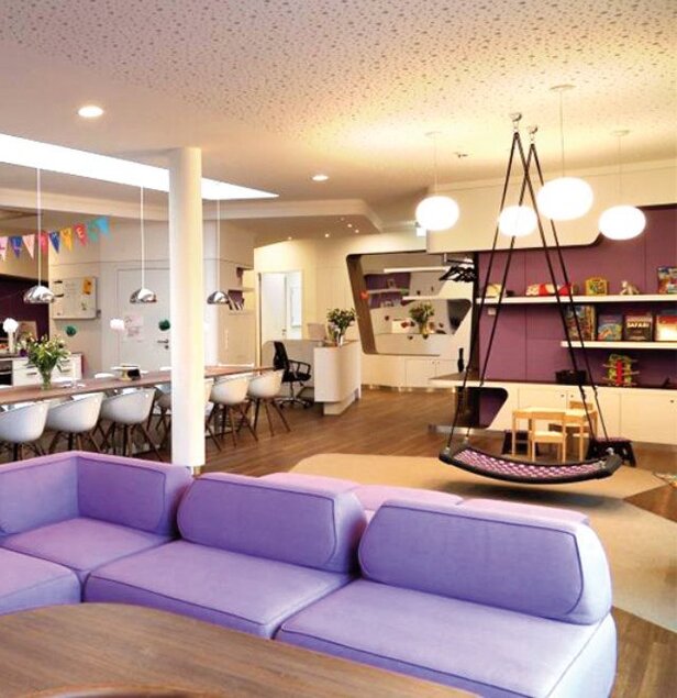 Moderný detský kútik s fialovým sedením a hojdačkou, navrhnutý pre pohodlie a kreativitu detí v prostredí McDonald's.