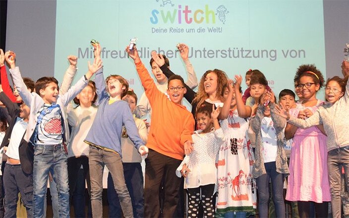 Děti radostně slaví na pódiu v rámci akce Switch, která podporuje globální povědomí a zapojení komunity.