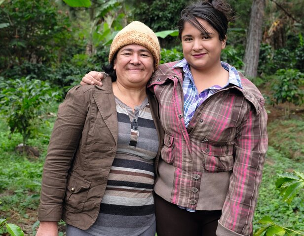 Zwei Frauen lächeln gemeinsam in einer üppigen Kaffeeplantage und fördern den Gemeinschaftsgeist und nachhaltige Anbaumethoden.