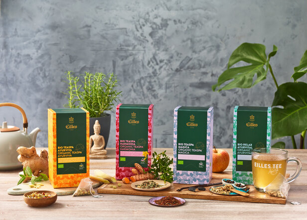 Das Bio-Spa-Sortiment von Eilles Tea wird auf einem rustikalen Tisch mit pflanzlichen Zutaten und einem Glas aufgebrühten Tees präsentiert.