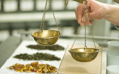 Osoba váží čaj na zlatých vahách.