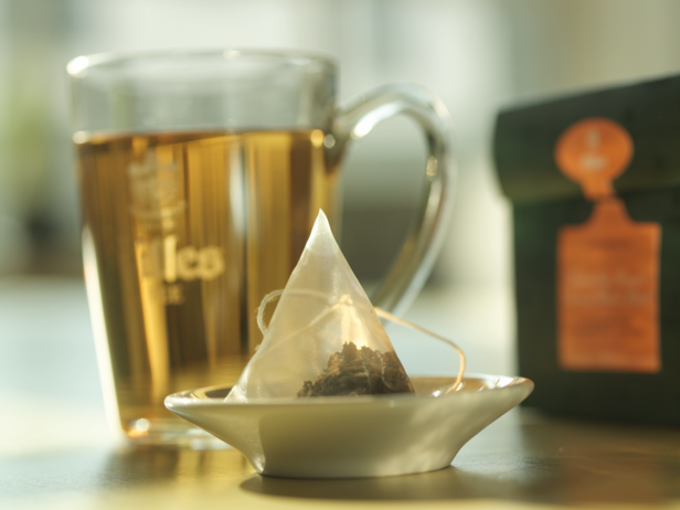 Przytulny zestaw zawierający torebkę herbaty ziołowej na spodku obok szklanki zaparzonej herbaty i jej opakowania.