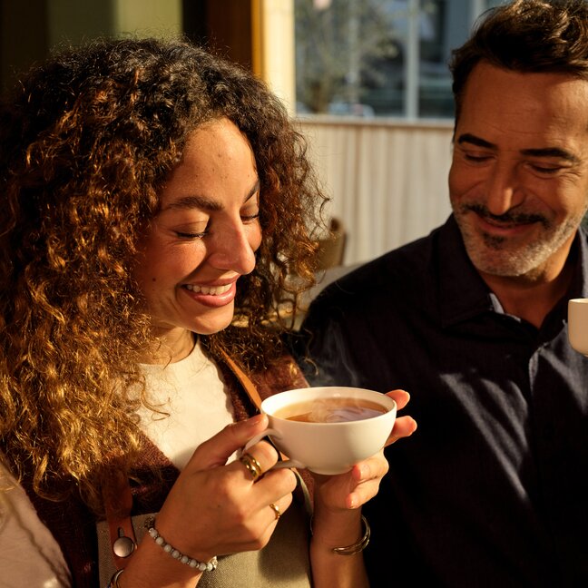 Freunde, die gemeinsam einen Kaffee genießen, lächeln in einem Café und zeigen einen fröhlichen Moment bei einem Eilles-Kaffee.
