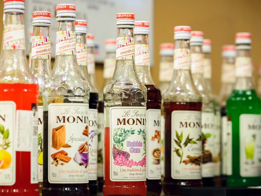 Różne butelki syropu Monin o żywych smakach, idealne do wzbogacania koktajli i deserów w barze.