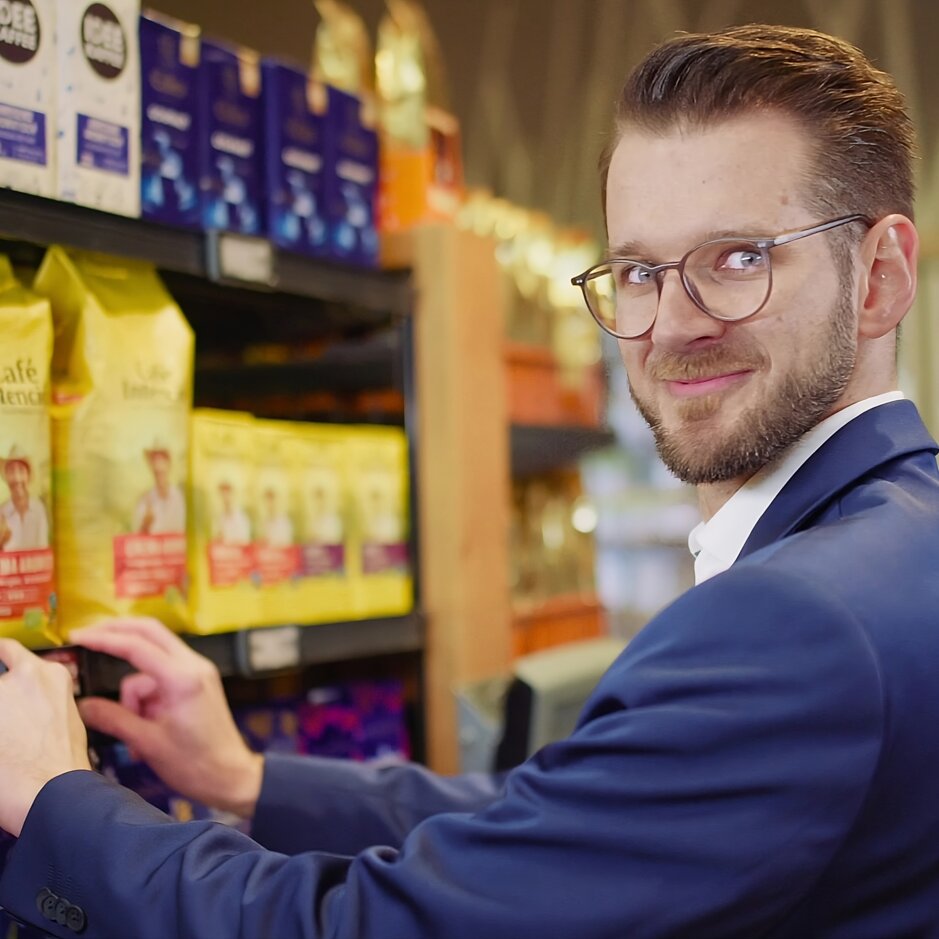 Man in a suit choosing coffee bags from a supermarket shelf, showcasing diverse coffee brands and products.