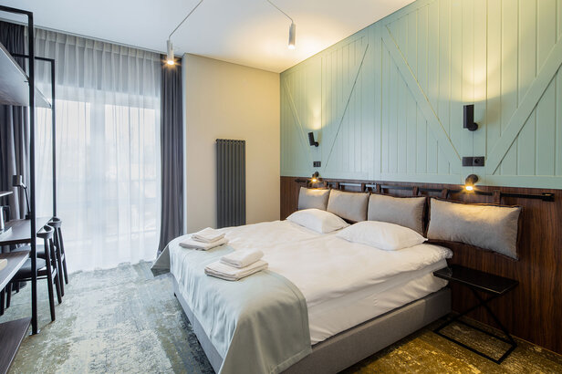 Nowoczesna sypialnia hotelowa z podwójnym łóżkiem, stylowym wystrojem i dużymi oknami z naturalnym światłem. Idealny na relaksujące pobyty.