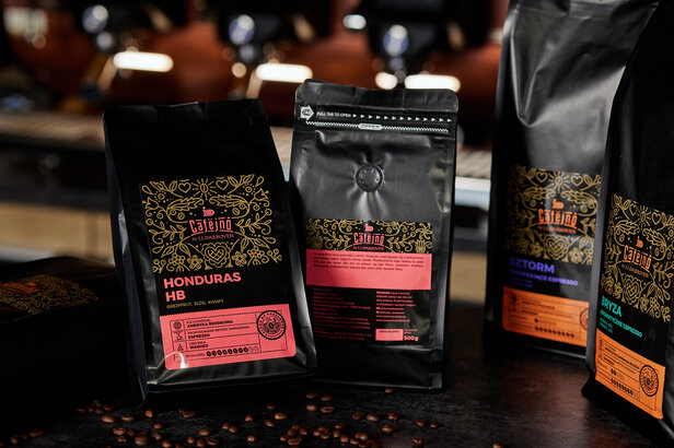 Torebki kawy Café Jno z mieszankami Honduras HB, Szstorm i Bryza w żywych opakowaniach na ciemnym blacie.