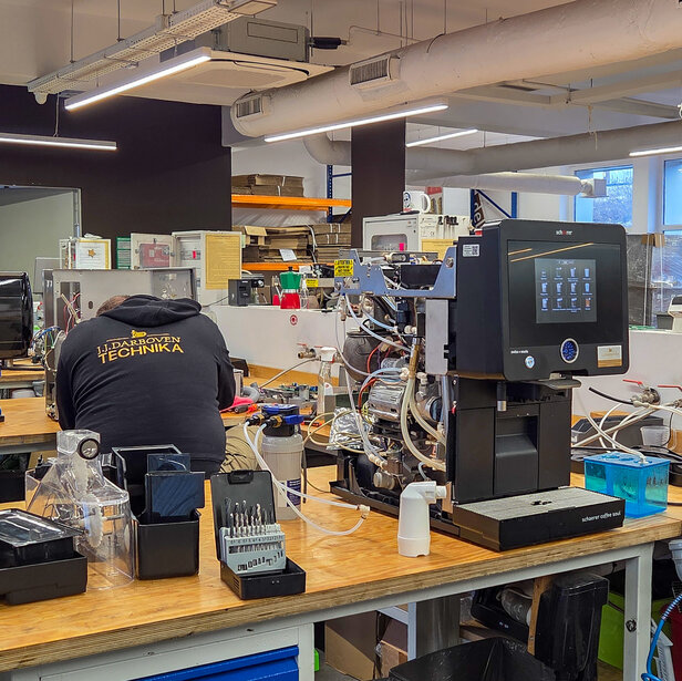 Technik naprawia ekspresy do kawy w ruchliwym warsztacie, prezentując narzędzia i sprzęt do konserwacji i serwisowania.