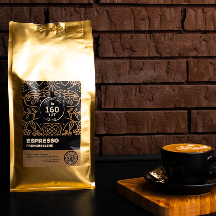 Złota torebka kawy espresso obok filiżanki kawy premium blend na drewnianej desce na tle ceglanej ściany.