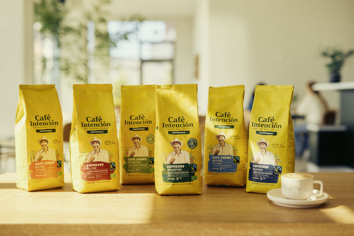 Die Verpackungen von Café Intención werden präsentiert und zeigen eine Vielzahl von Produkten vor dem Hintergrund einer Tasse Kaffee in einer hellen Café-Atmosphäre.