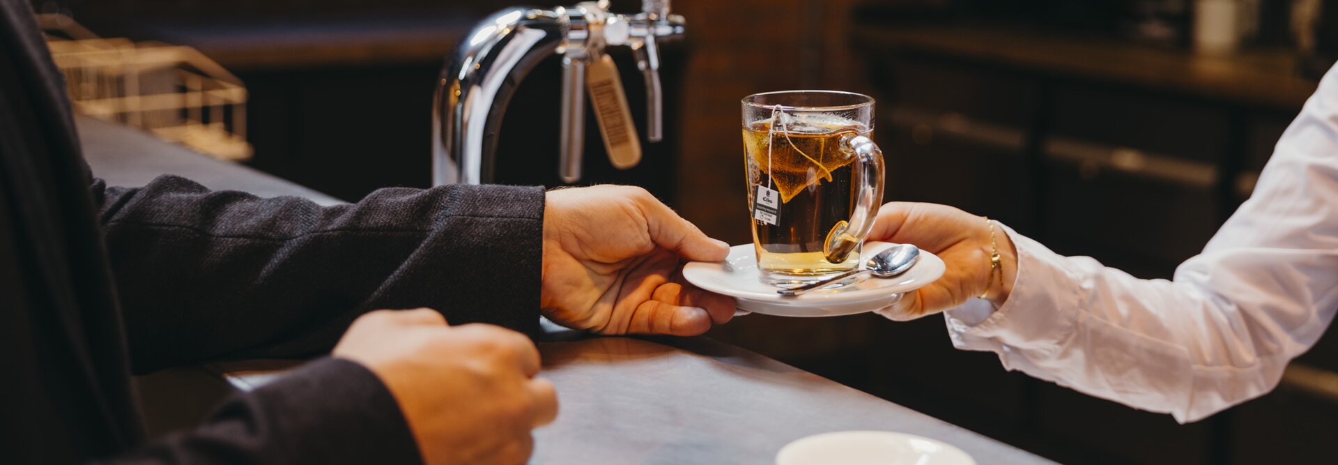 A barista serves a steaming cup of tea to a customer at a modern café, highlighting a warm beverage experience.